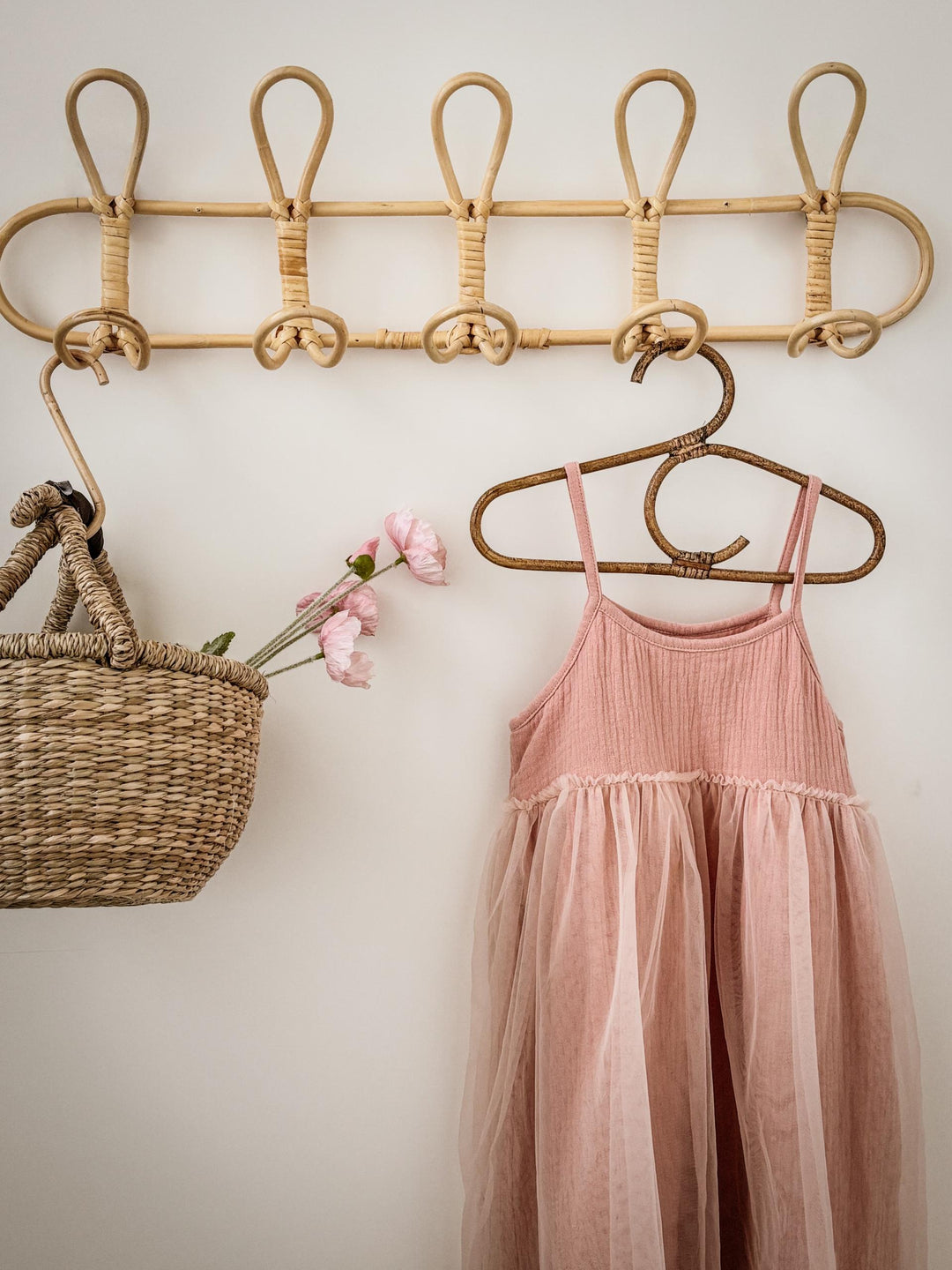 Pink dress hanging on a rattan hanger with a basket and flowers on a light background