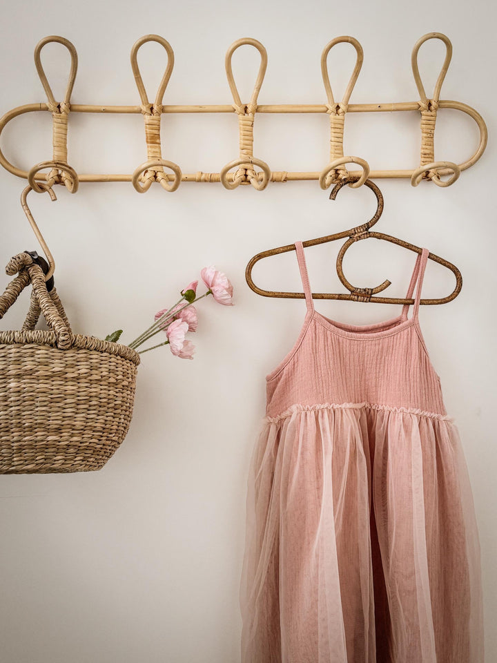 Pink dress hanging on a rattan hanger with a basket and flowers on a light background